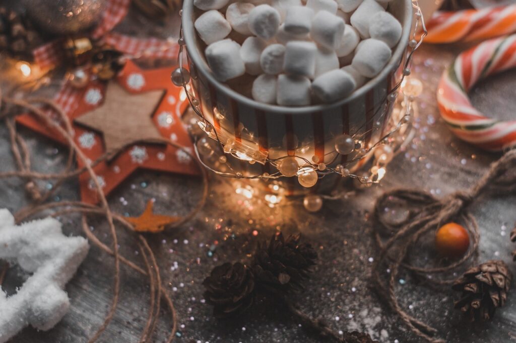 cup of hot cocoa with mini marshmallows sitting on a table covered in twinkle lights and candy canes