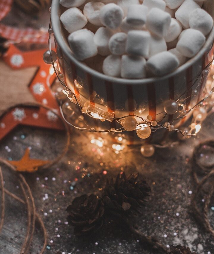 cup of hot cocoa with mini marshmallows sitting on a table covered in twinkle lights and candy canes